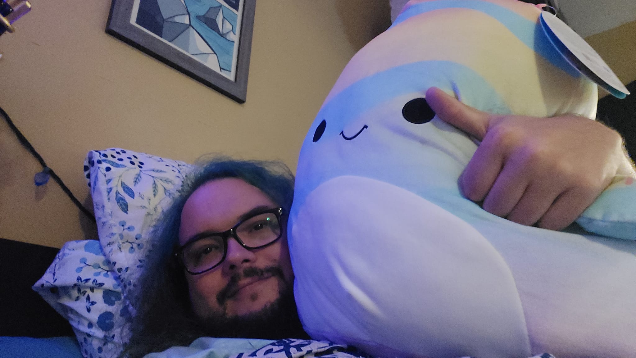 A man with green hair laying with a large Squishmallow fish, Photo 1